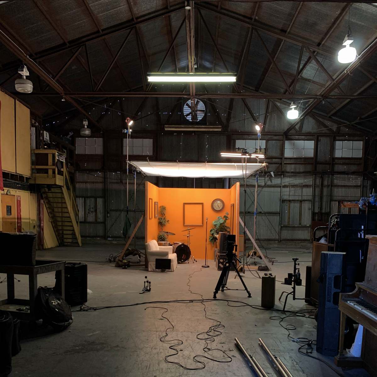 An empty industrial space features a backdrop of orange, with a small sofa, plants, and cameras set up for a photoshoot.
