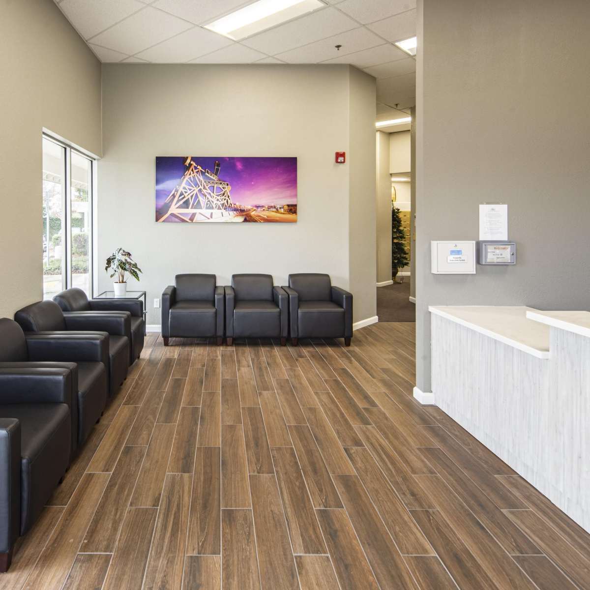 A modern waiting area with black chairs, a wooden floor, and a bright wall with a colorful artwork above a reception desk.