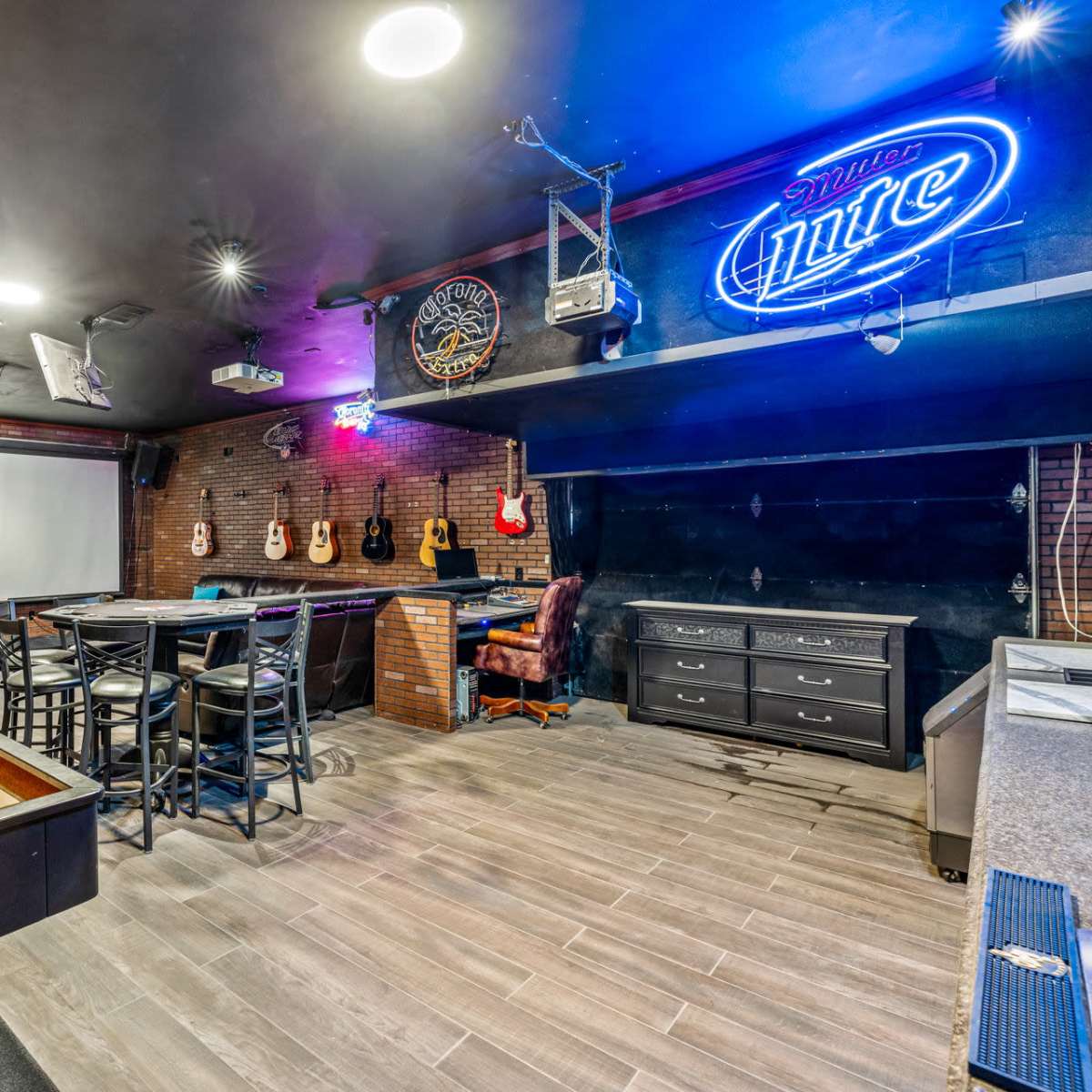 A finished basement entertainment space with a shuffleboard table, bar area, and a projection screen surrounded by guitars on the wall.