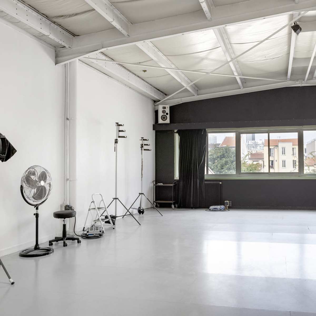 A spacious, minimally furnished photography studio with large windows and various equipment arranged along the walls.