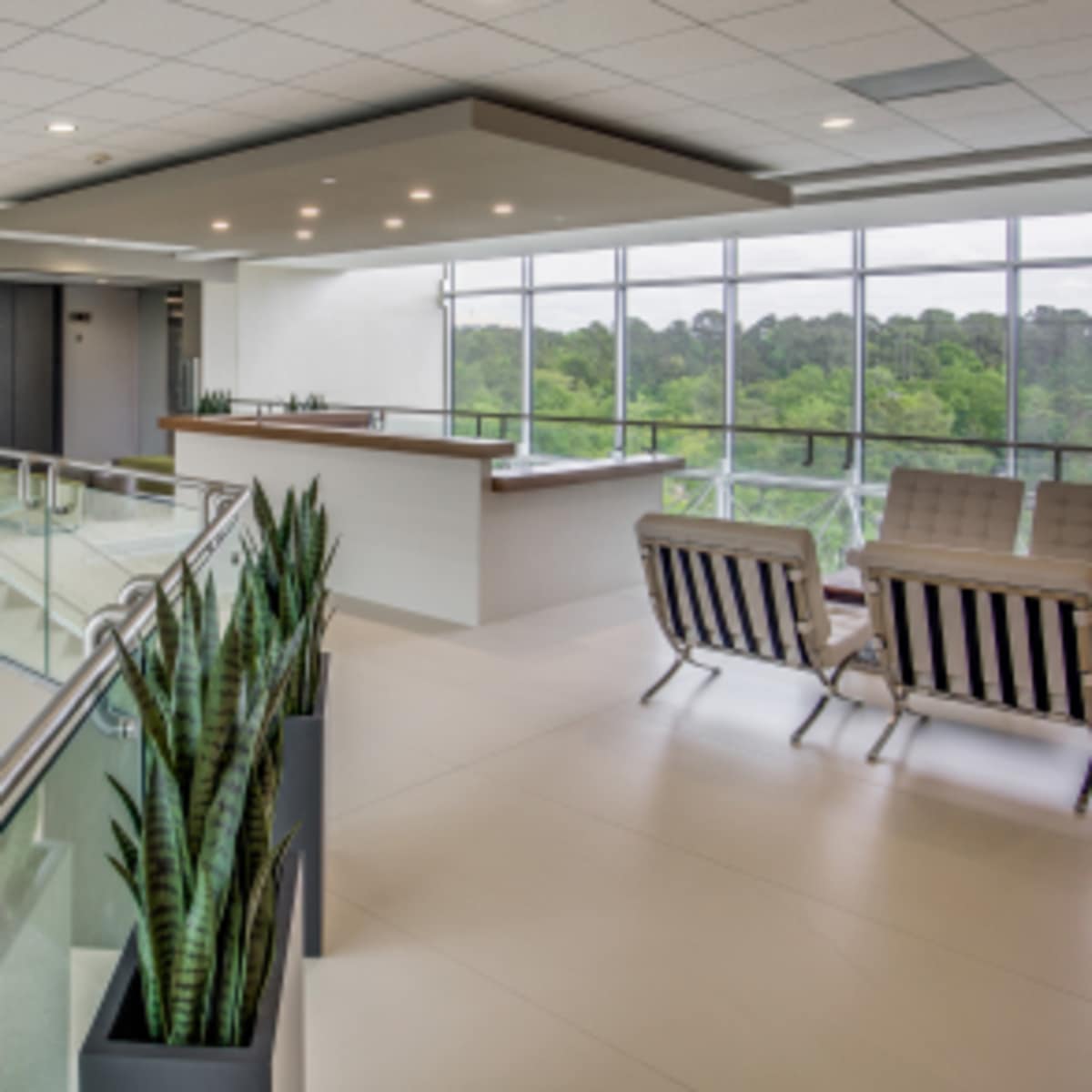 A modern atrium with large windows, a staircase, and seating areas overlooking greenery.