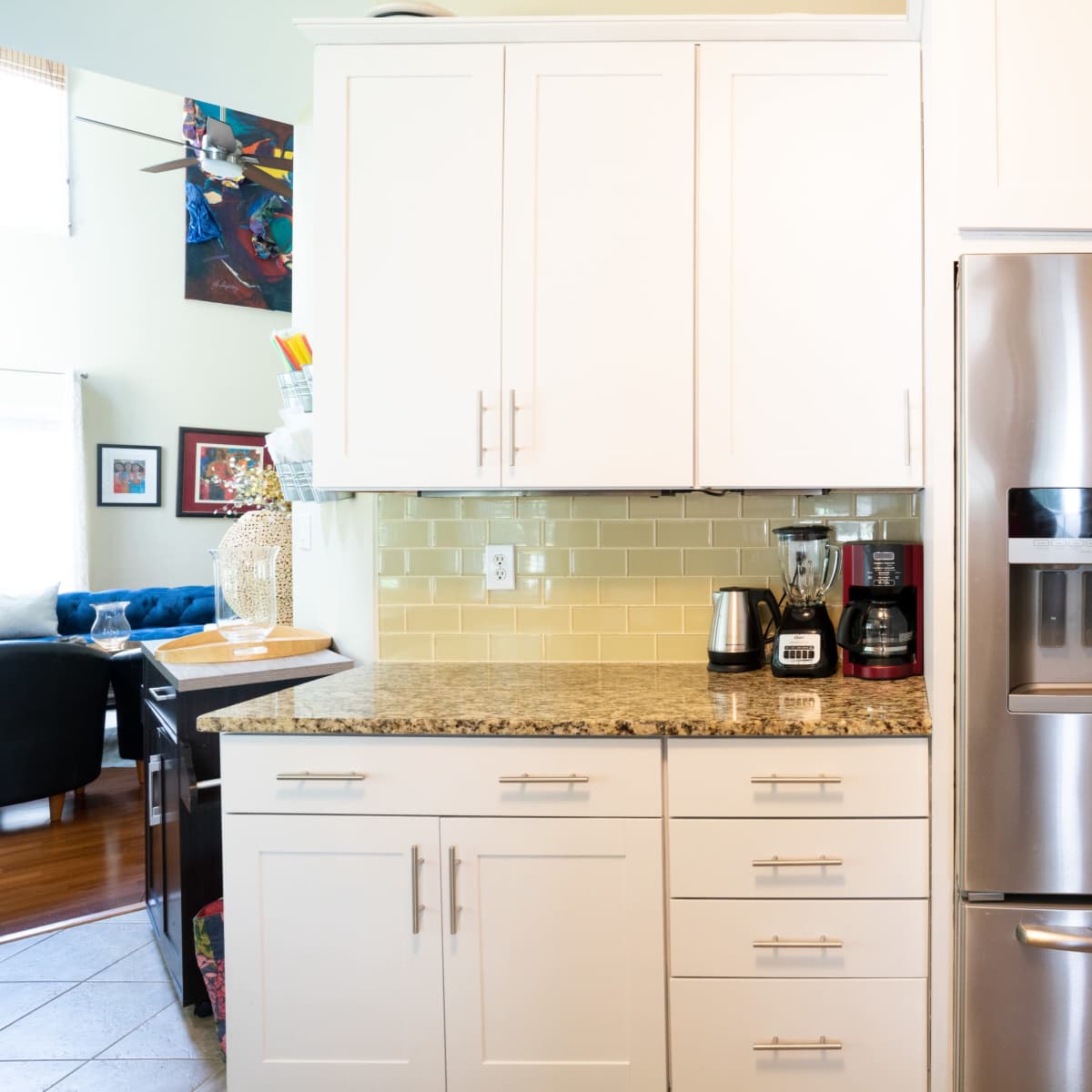 A modern kitchen featuring white cabinetry, a stainless steel refrigerator, and a granite countertop with small appliances.