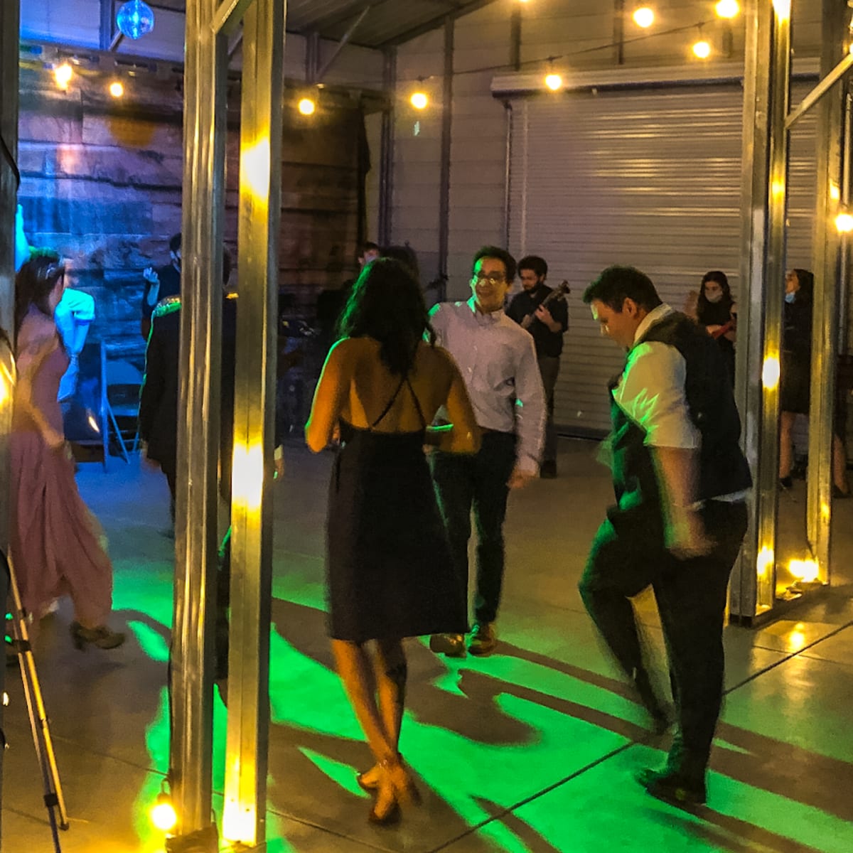 A group of people dances under string lights in a large indoor space with colorful lighting.
