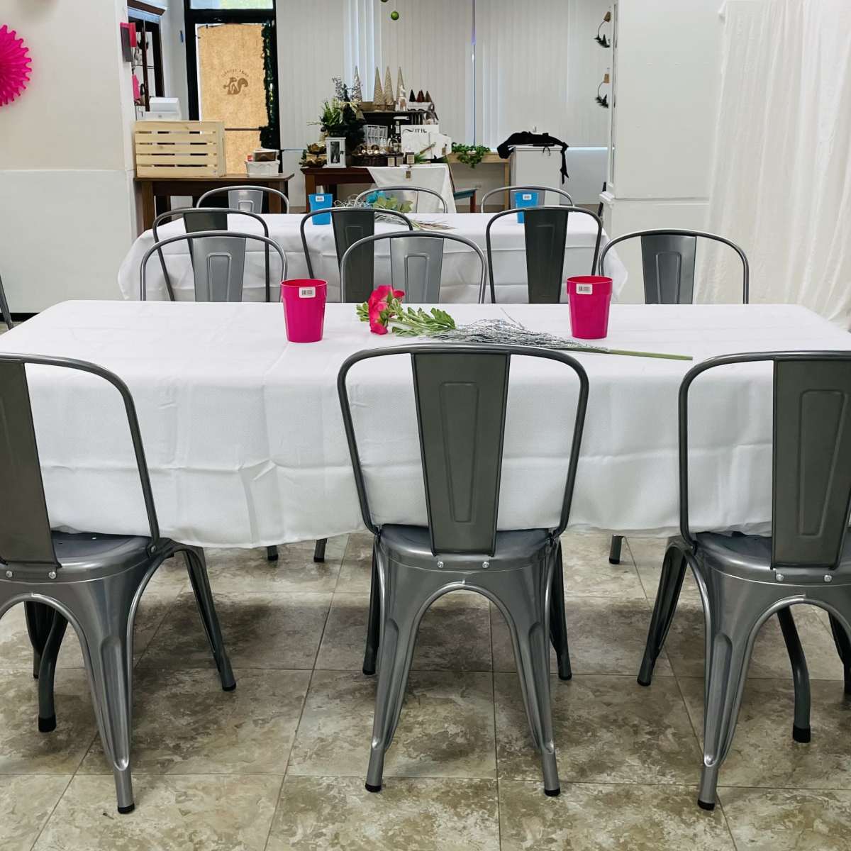 A large table is set with a white tablecloth and surrounded by metal chairs in a spacious room.
