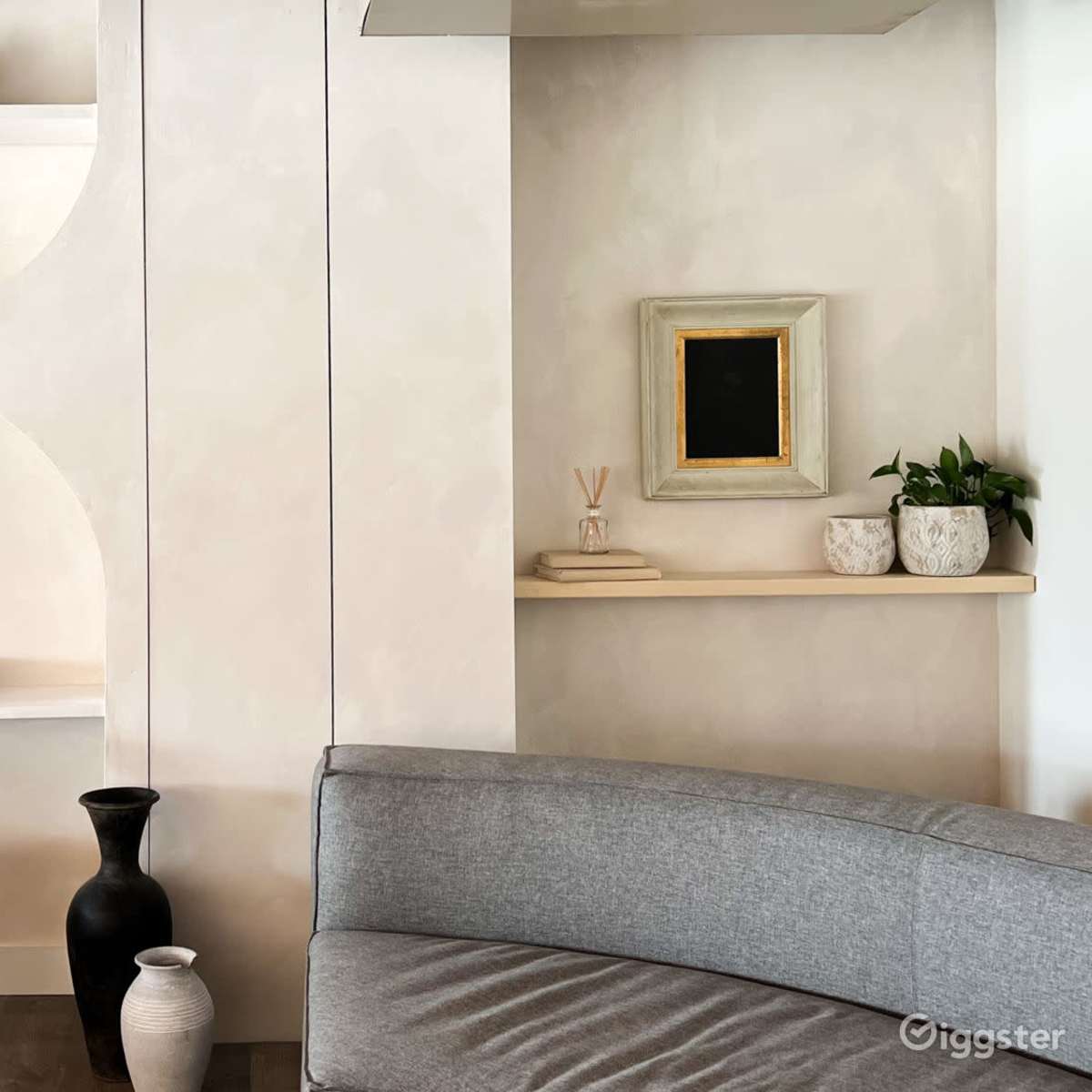 A modern interior with a curved shelf design, a gray sofa, and various decorative objects including a black vase and framed artwork.