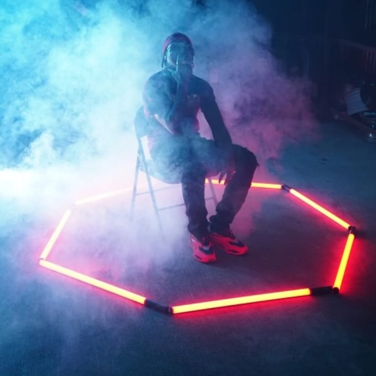 A person sits on a chair inside a glowing hexagon formed by neon lights, surrounded by a misty atmosphere.