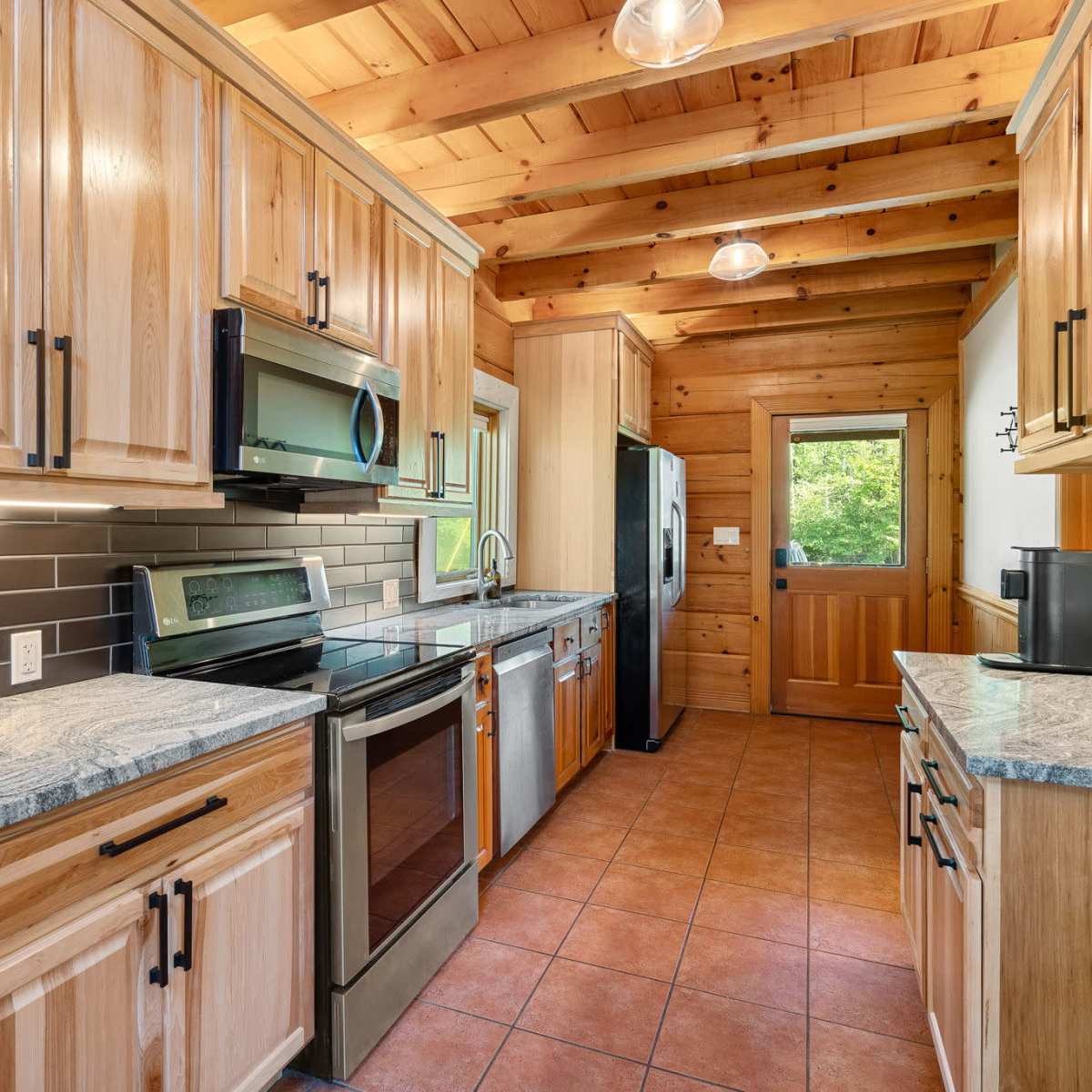 A kitchen features wooden cabinets, granite countertops, stainless steel appliances, and a tile backsplash, with natural light coming from a nearby window.