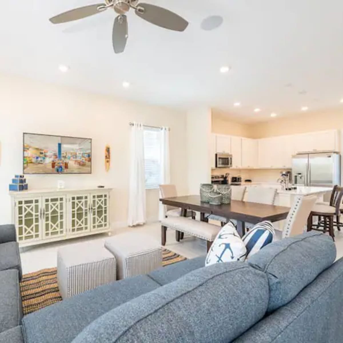 A living room with a sectional sofa, a television on the wall, and a dining area connected to a kitchen with modern appliances.