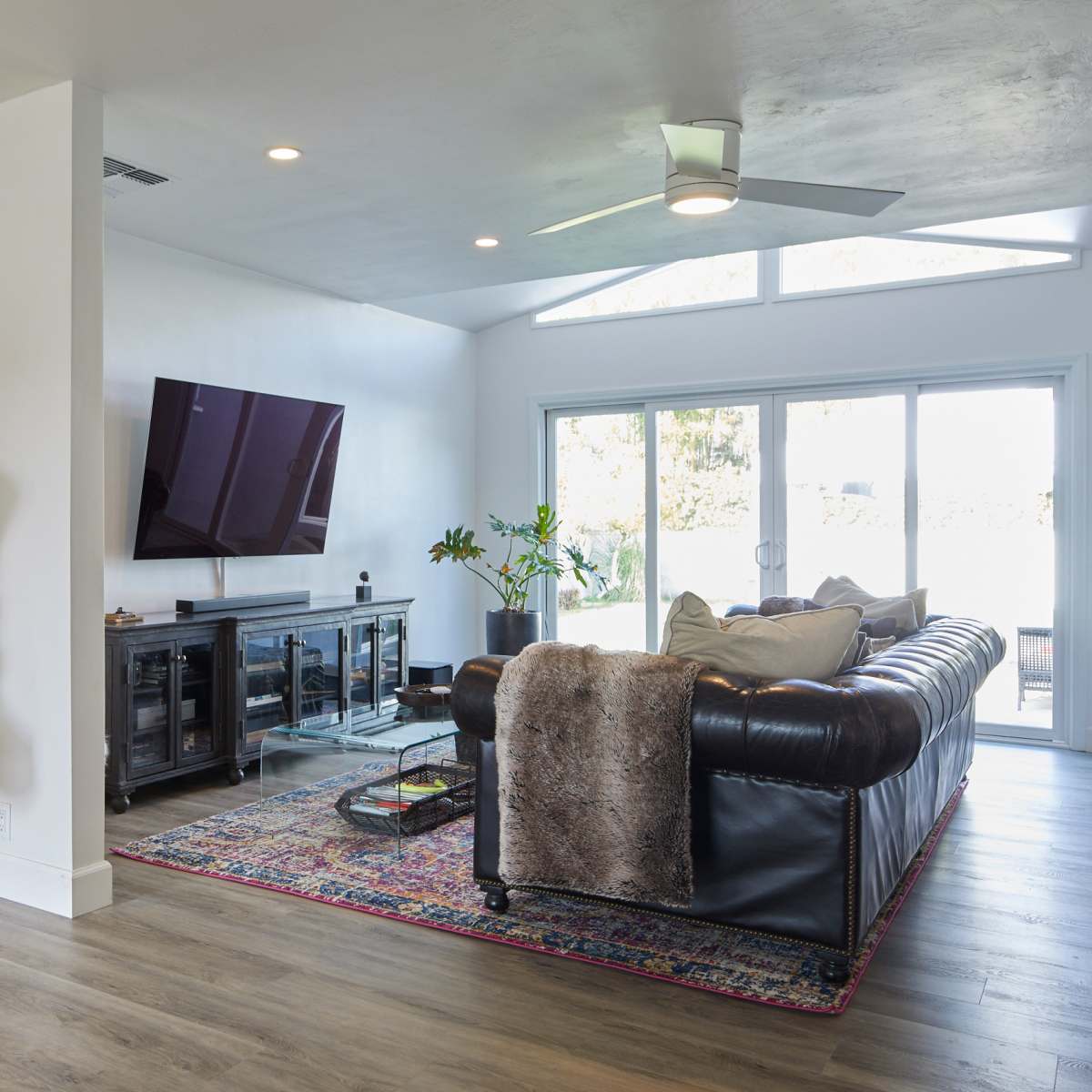 A modern living room featuring a leather sofa, a large television mounted on the wall, and a decorative wooden sculpture in a bright, airy space.
