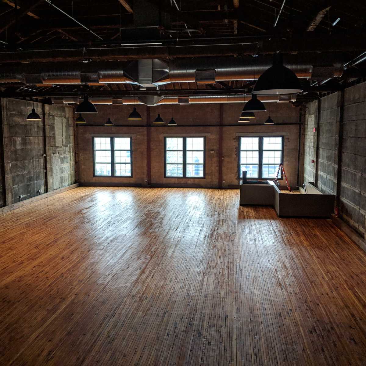 An empty industrial space with wooden floors, large windows, and exposed concrete walls.