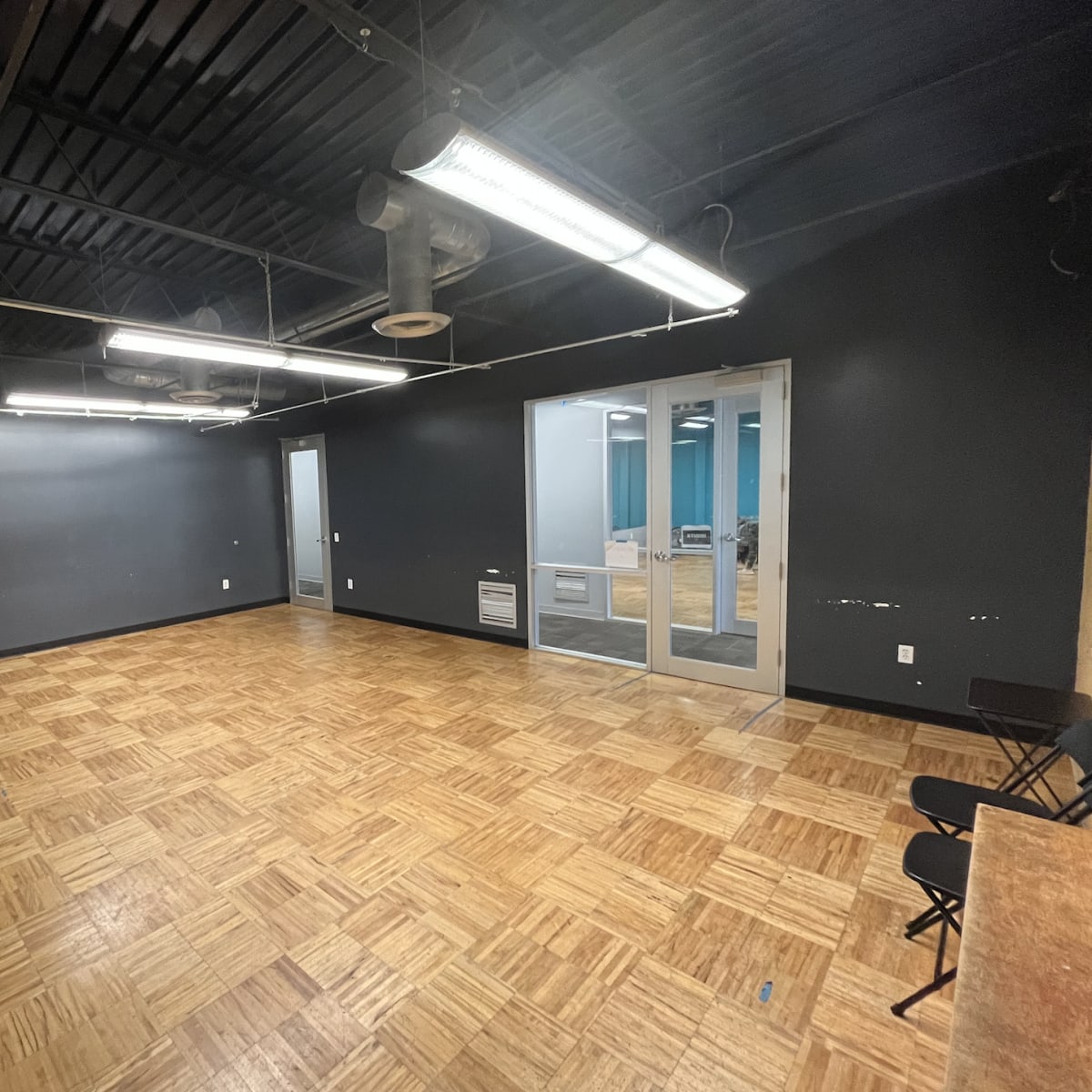 A spacious room with dark walls, a wooden floor, and a large mirror on one side, featuring a glass door that leads to an adjacent area.