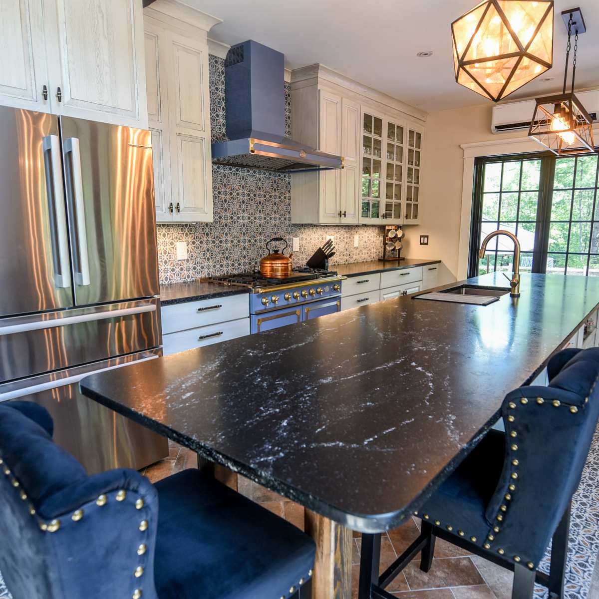 A modern kitchen features a large island with dark countertops, stainless steel appliances, and cabinetry with white and blue accents.
