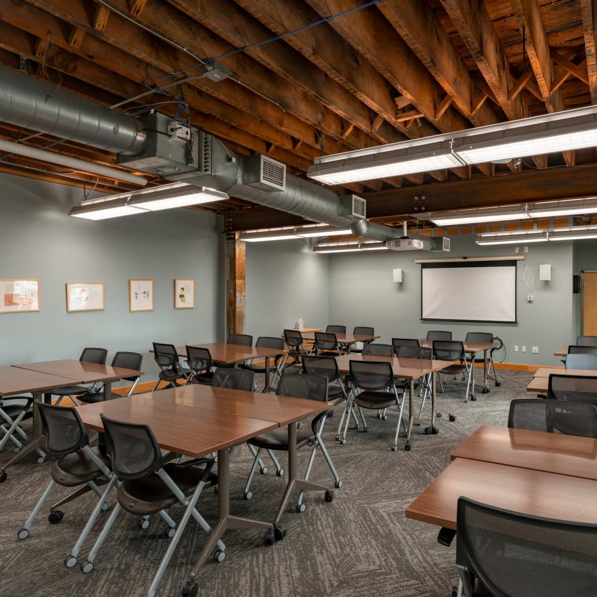 A modern classroom features multiple tables and chairs arranged for a collaborative learning environment, with exposed beams and brick walls.