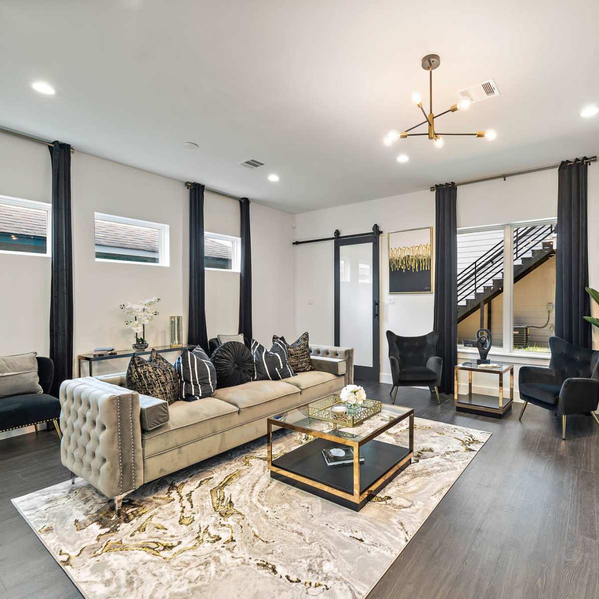 The living room features a light-colored sectional sofa, a glass coffee table on a patterned rug, and dark curtains framing large windows.