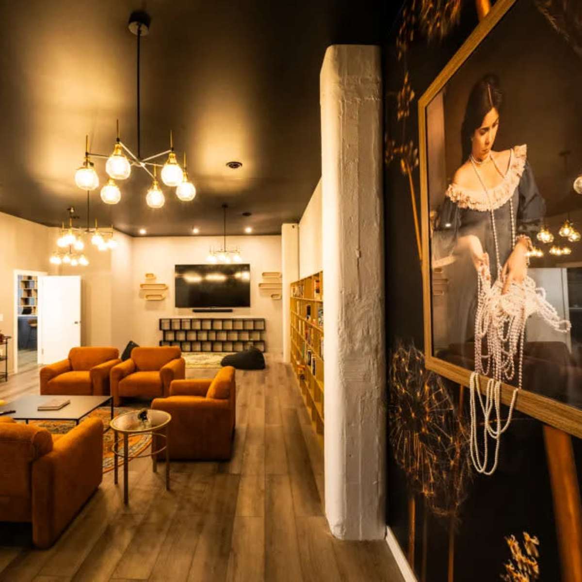 A modern lounge area with orange sofas, decorative lighting, and a large wall mural of a woman wearing pearls.
