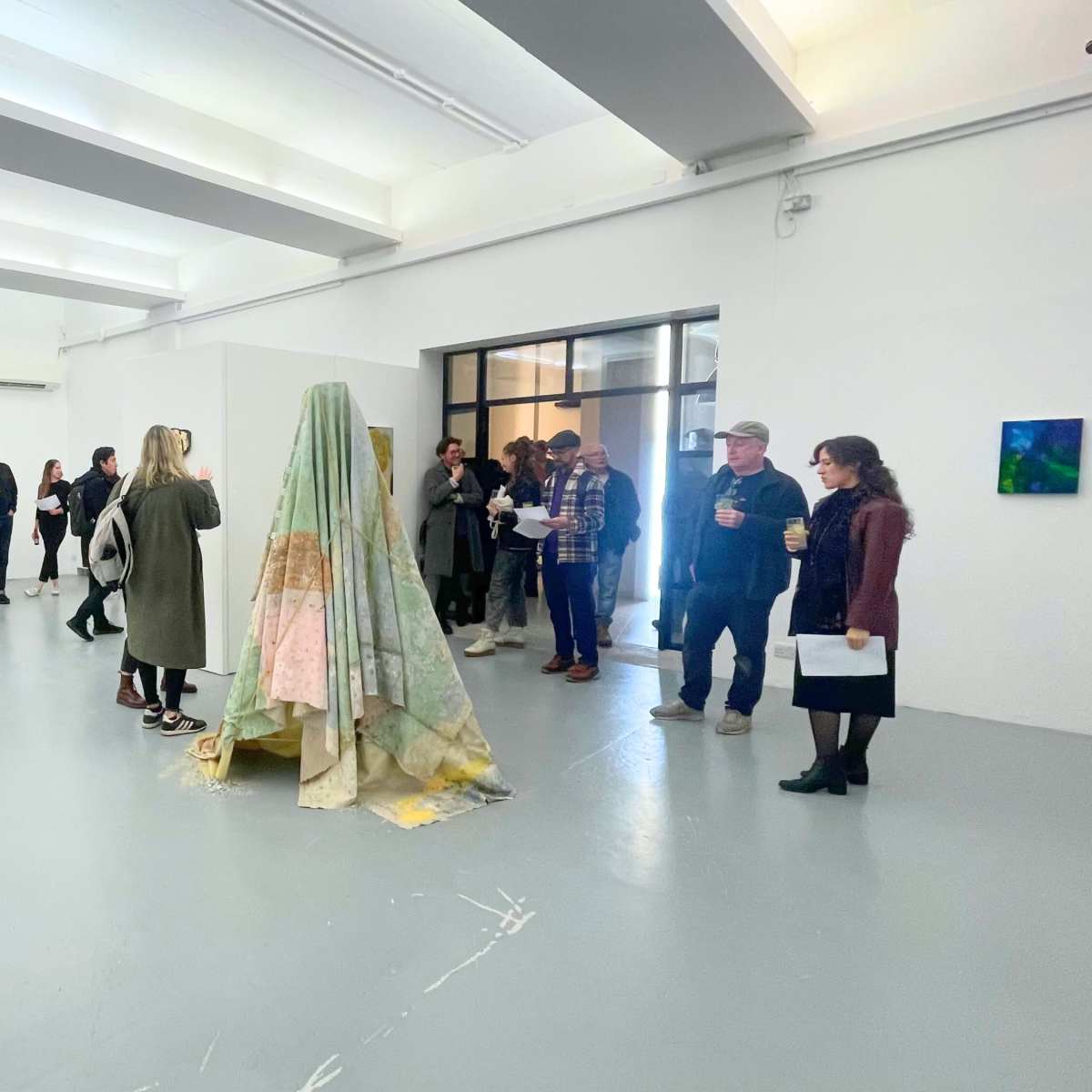 A group of people interacts in an art gallery featuring various artworks displayed on the walls and sculptures in the center of the room.