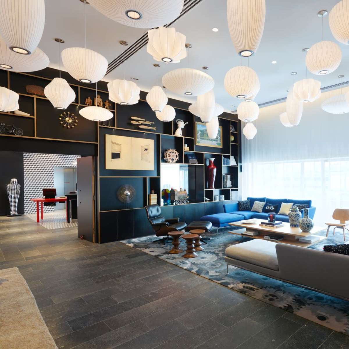 A modern interior space with varied seating arrangements, decorative wall art, and numerous hanging light fixtures.