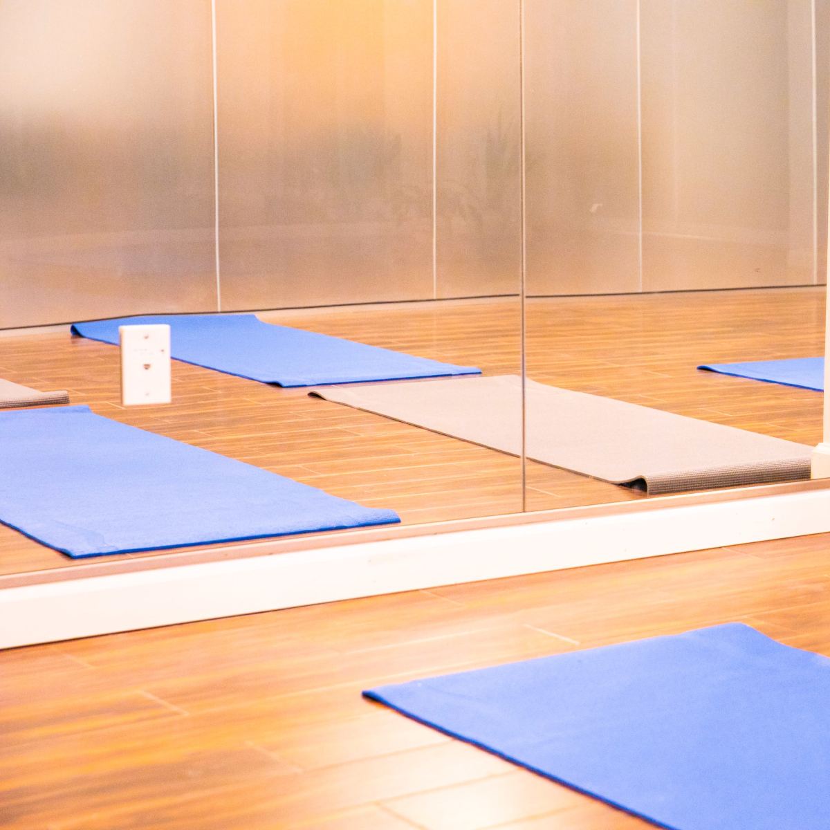 Several yoga mats arranged on a wooden floor in front of a mirrored wall.