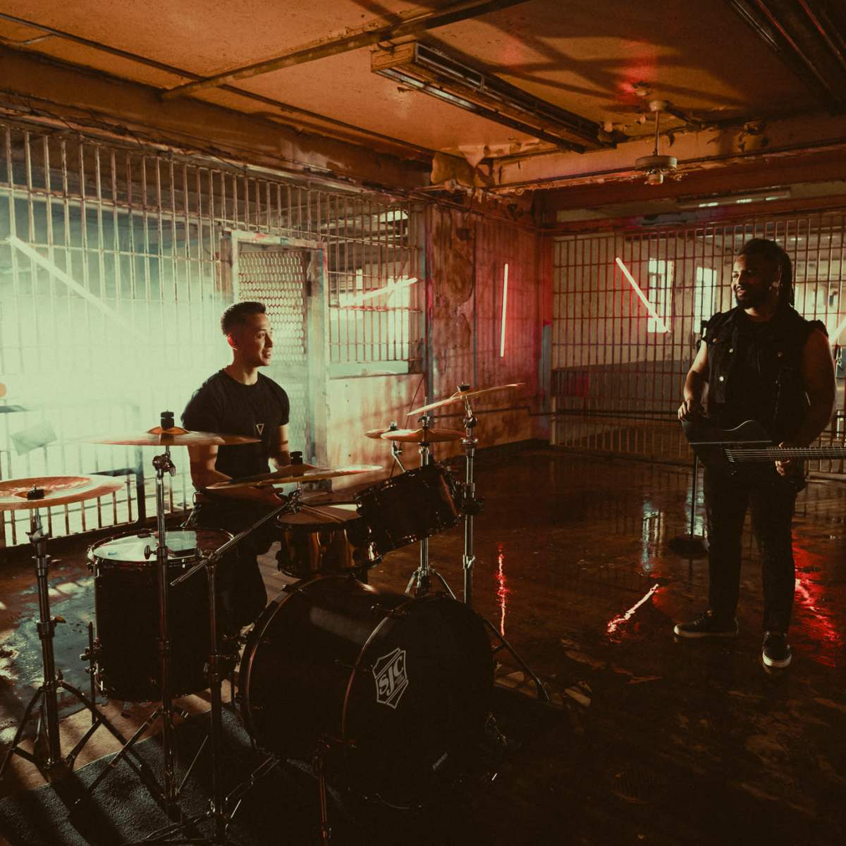A band performs in an industrial space with bright neon lighting and a grungy floor.