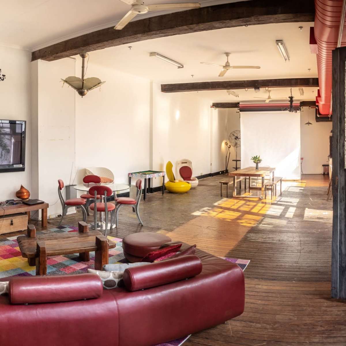 A spacious, well-lit living area with wooden floors, a large red couch, a television, and various seating arrangements.