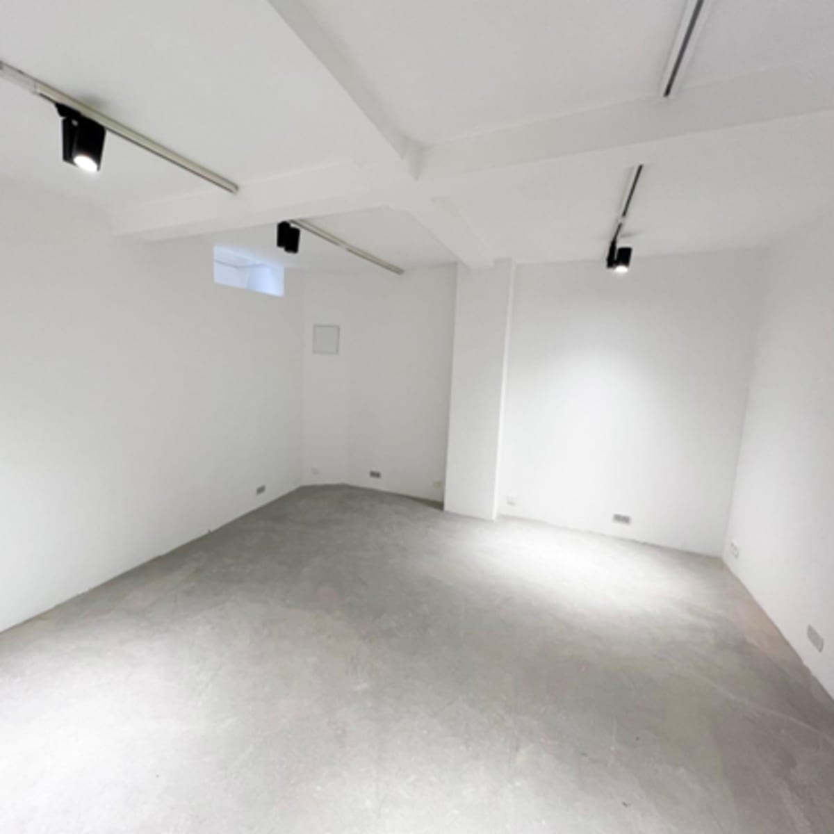 A bare white room with concrete flooring and overhead lights.