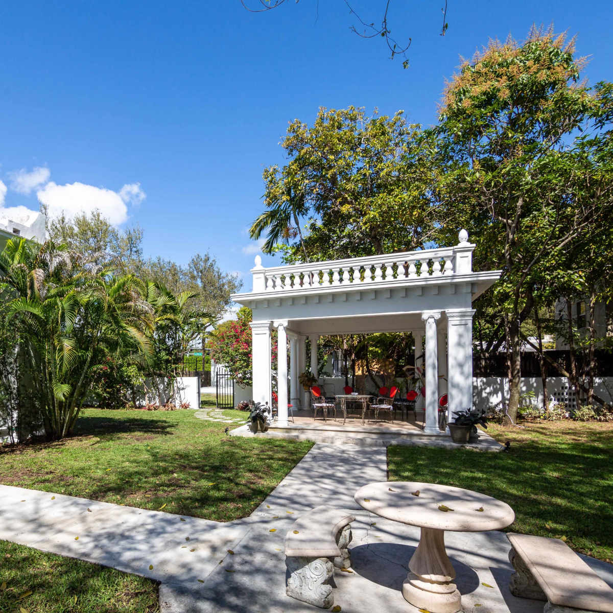 A landscaped backyard featuring a gazebo with seating, surrounded by manicured grass and tropical plants.