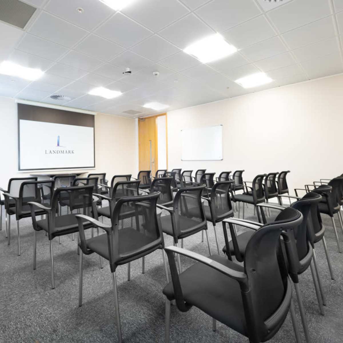 A conference room with rows of black chairs facing a projector screen and whiteboards.