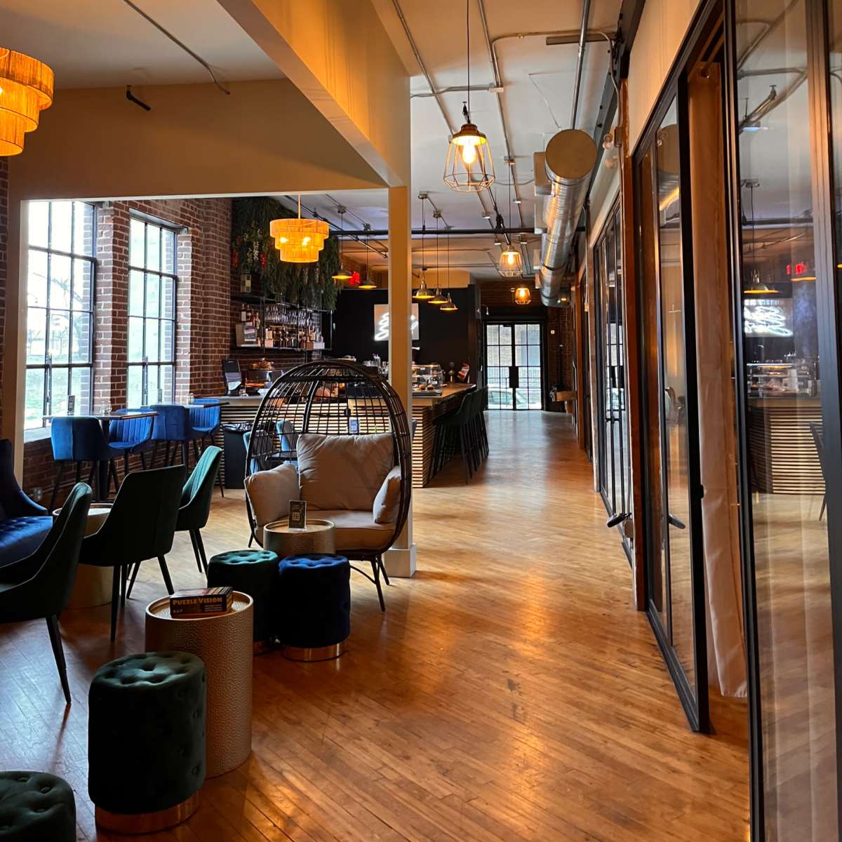 A modern interior of a spacious café or lounge with wooden floors, large windows, and various seating areas.