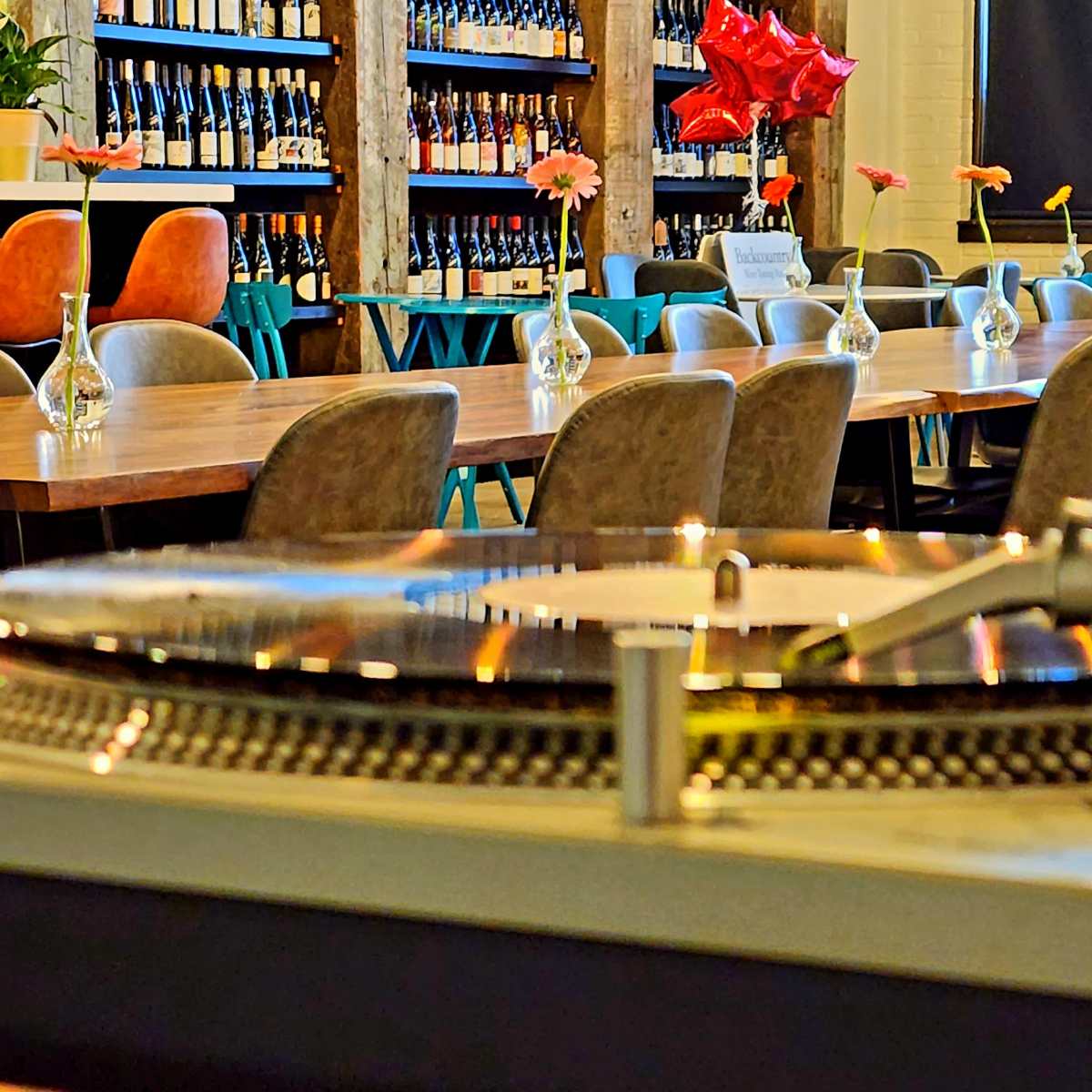 A close-up view of a turntable in the foreground, with a spacious restaurant setting featuring a long table and decorative flowers in vases in the background.