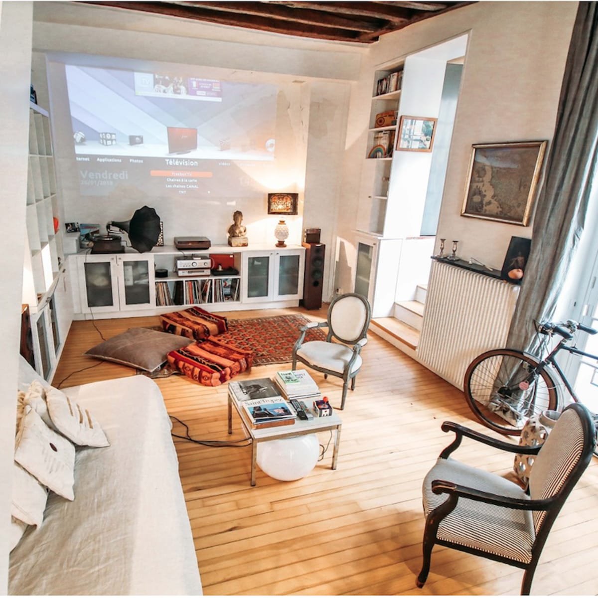 A cozy living room features a white sofa, an assortment of decor on the shelves, and a projection screen displaying content on the wall.