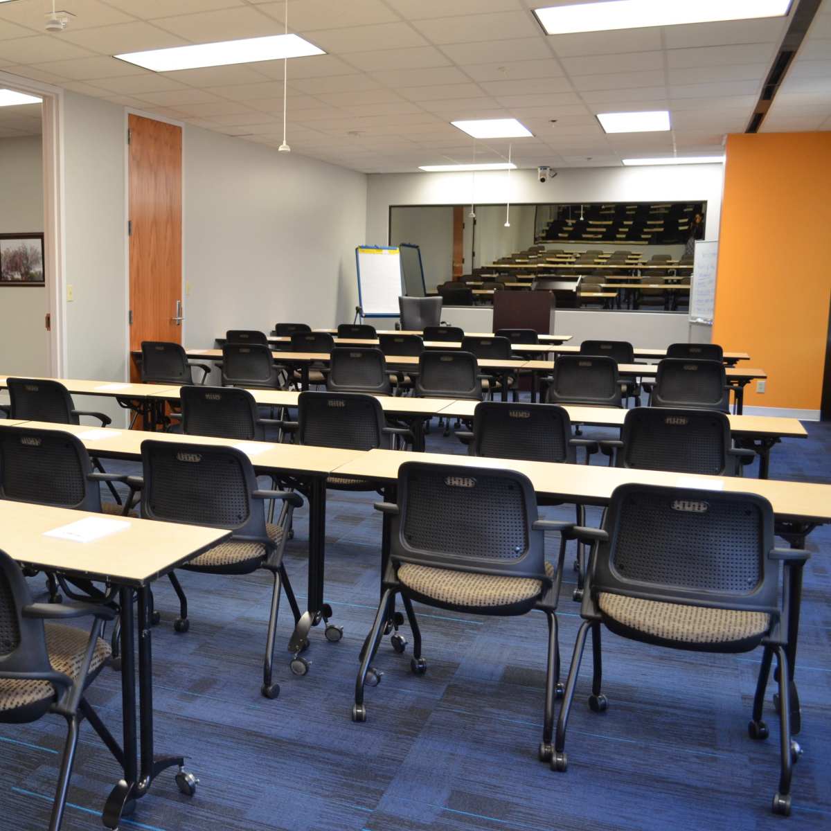 A classroom setting with multiple rows of tables and chairs arranged for a meeting or training session.