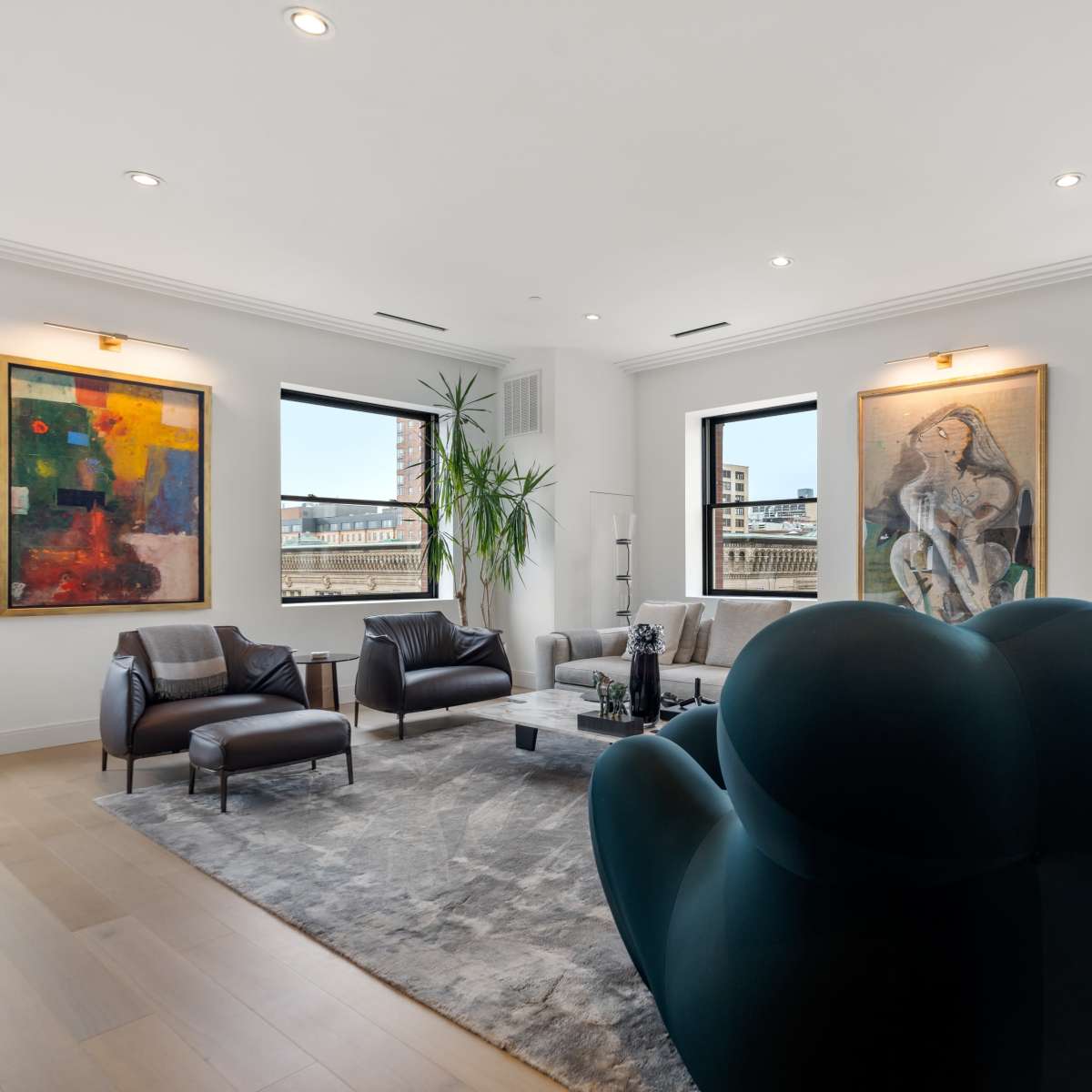 The room features modern furniture, large windows with urban views, and two abstract paintings on the walls.