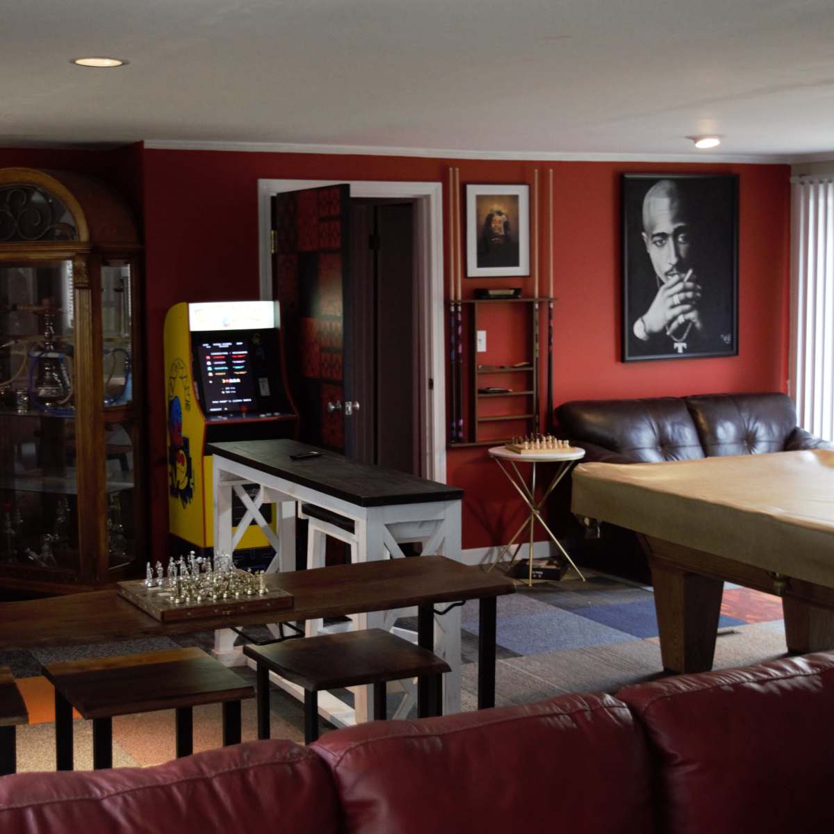 A cozy interior space featuring a game table, a chess set, a vintage arcade machine, and a colorful wall display with artwork.