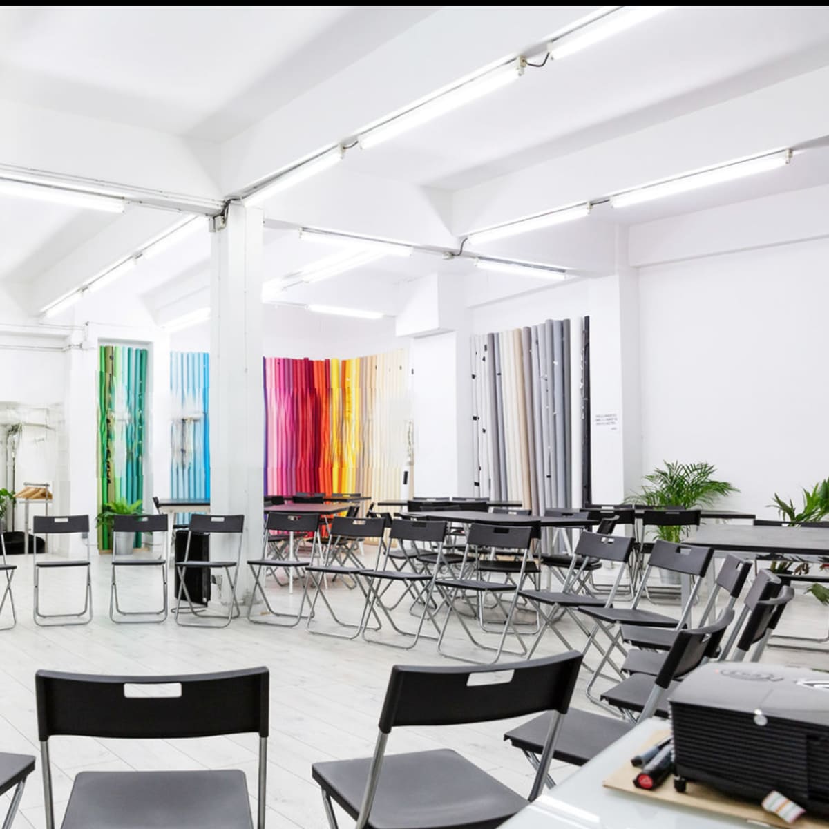 A spacious room with a circular arrangement of black folding chairs surrounding colorful vertical panels on the walls.