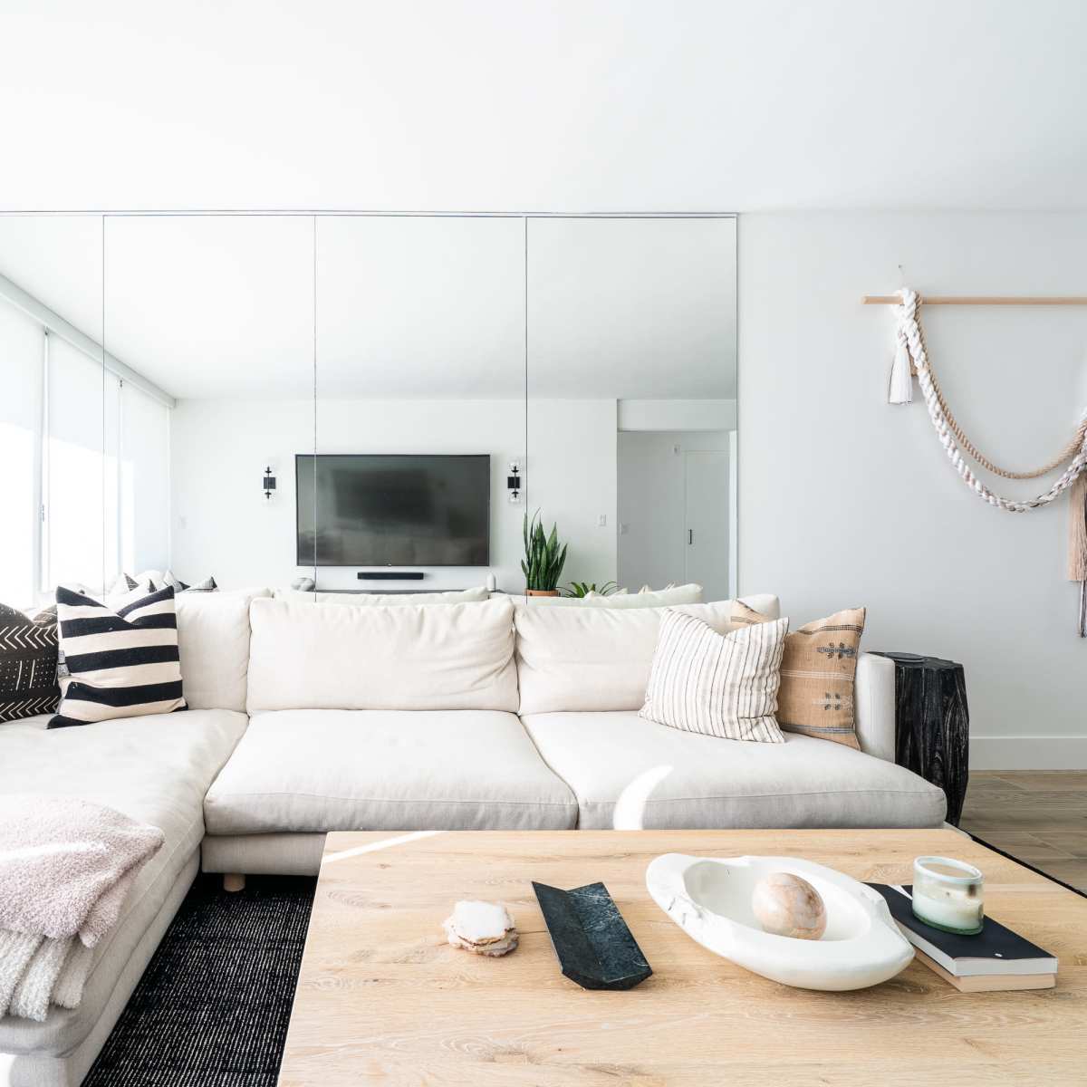 A modern living room with a large white sectional sofa, a wooden coffee table, and a wall-mounted television reflected in a mirror.
