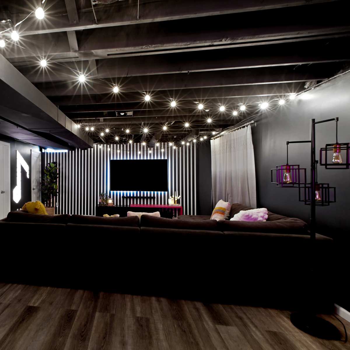 A modern living space with a sectional couch, decorative lighting, and a wall-mounted TV surrounded by vertical stripes.