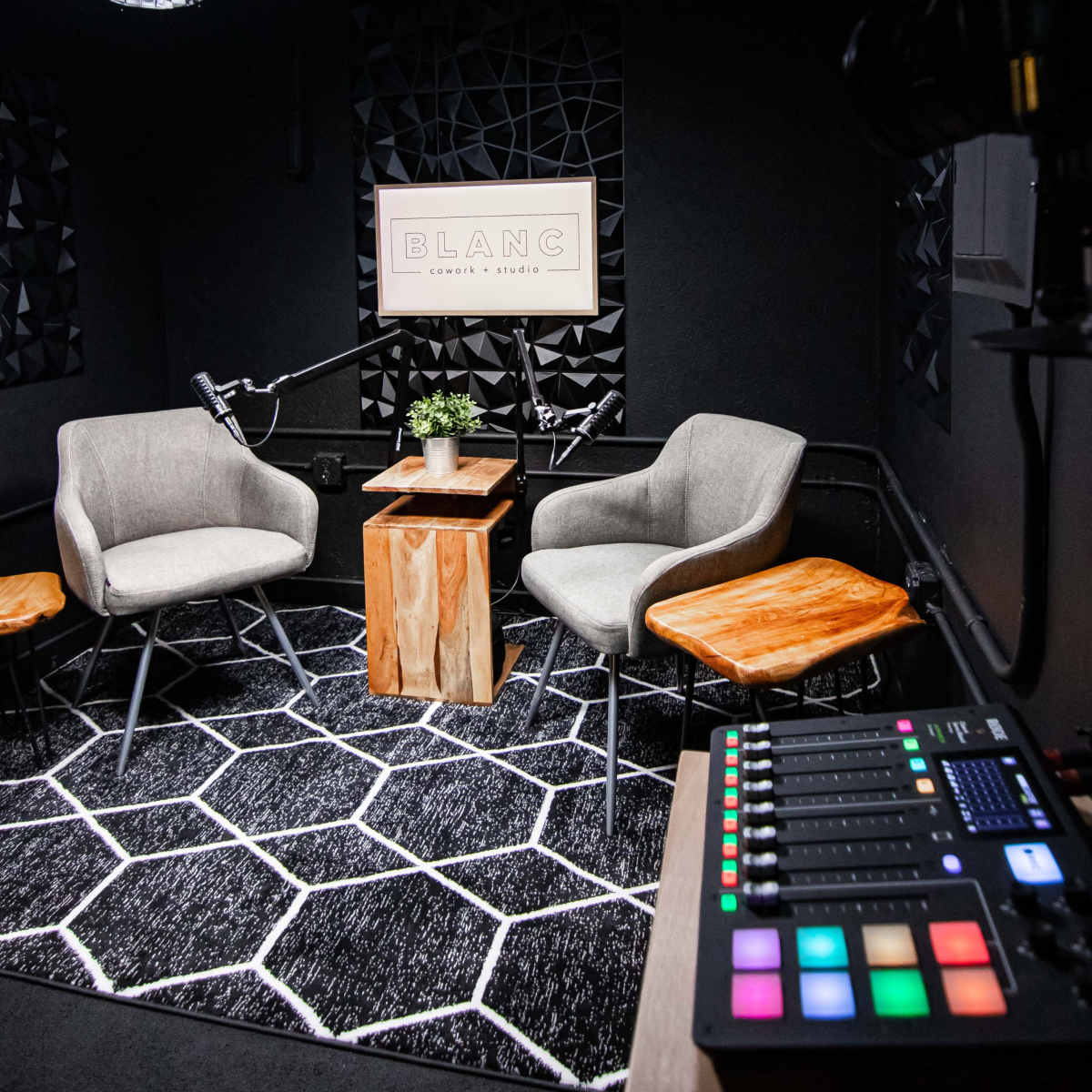 A modern podcast studio featuring two chairs, a wooden table, and lighting fixtures, with audio equipment in the foreground.
