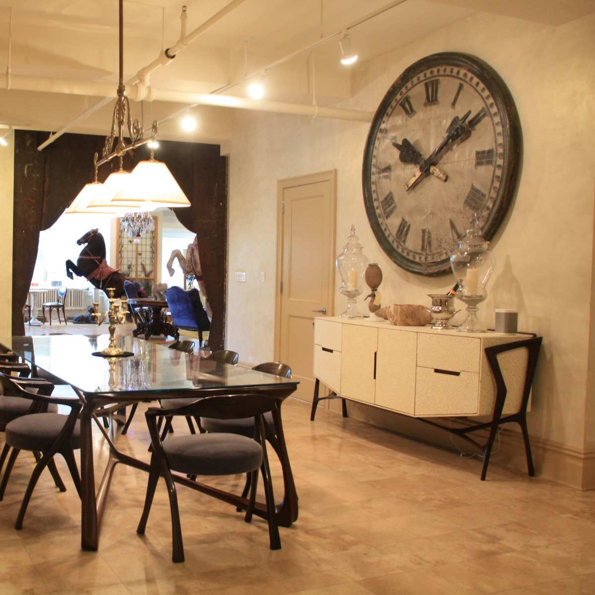 A dining room features a large table surrounded by chairs, a decorative wall clock, and various artwork and sculptures.