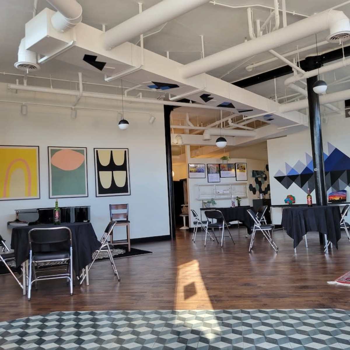 A spacious room with several tables covered in black cloth, surrounded by artwork on the walls and patterned flooring.