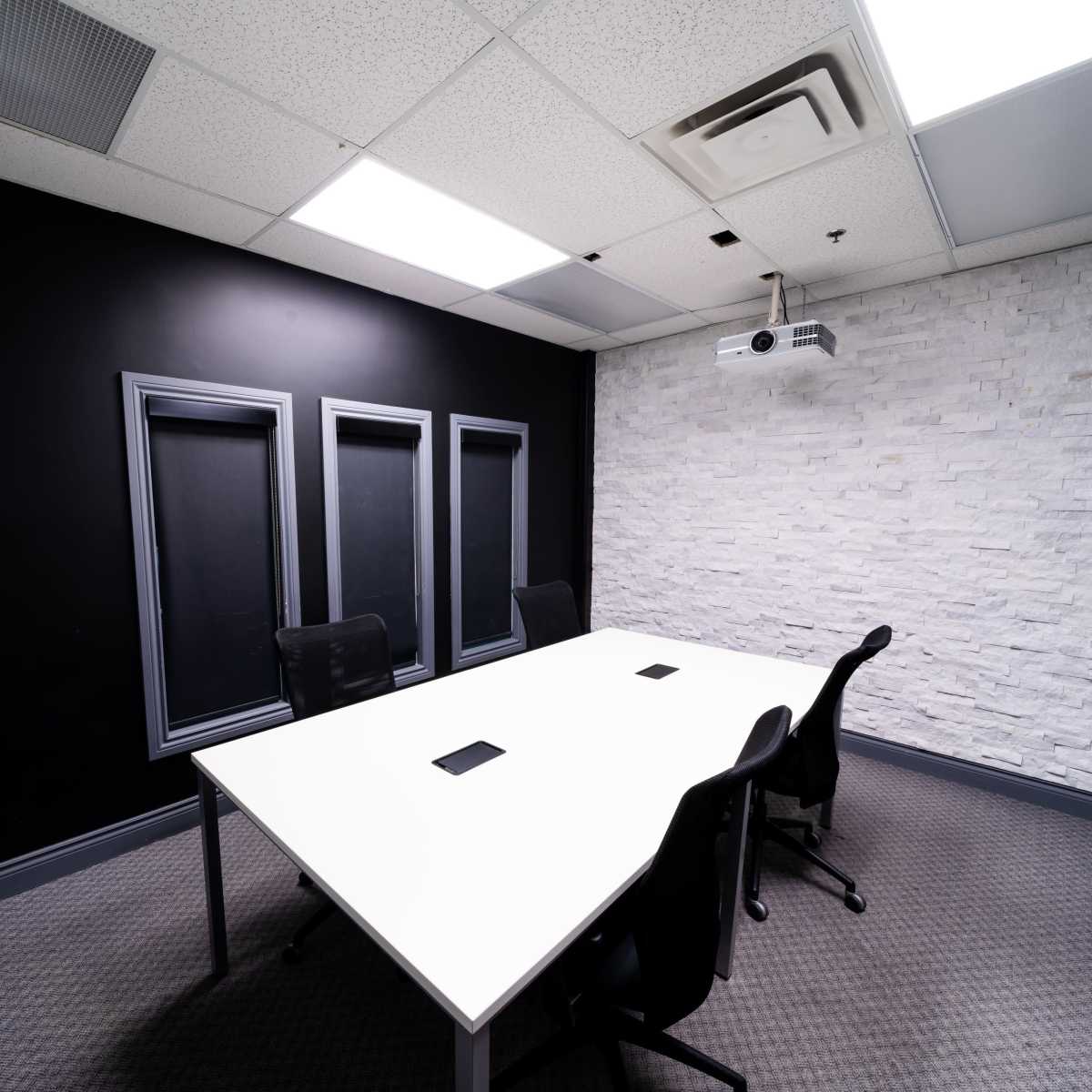 A modern conference room featuring a white table surrounded by black chairs, with black and stone-paneled walls.
