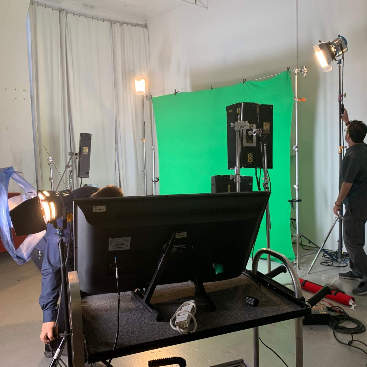 A filming setup features a green screen, lighting equipment, and a monitor in a studio environment.