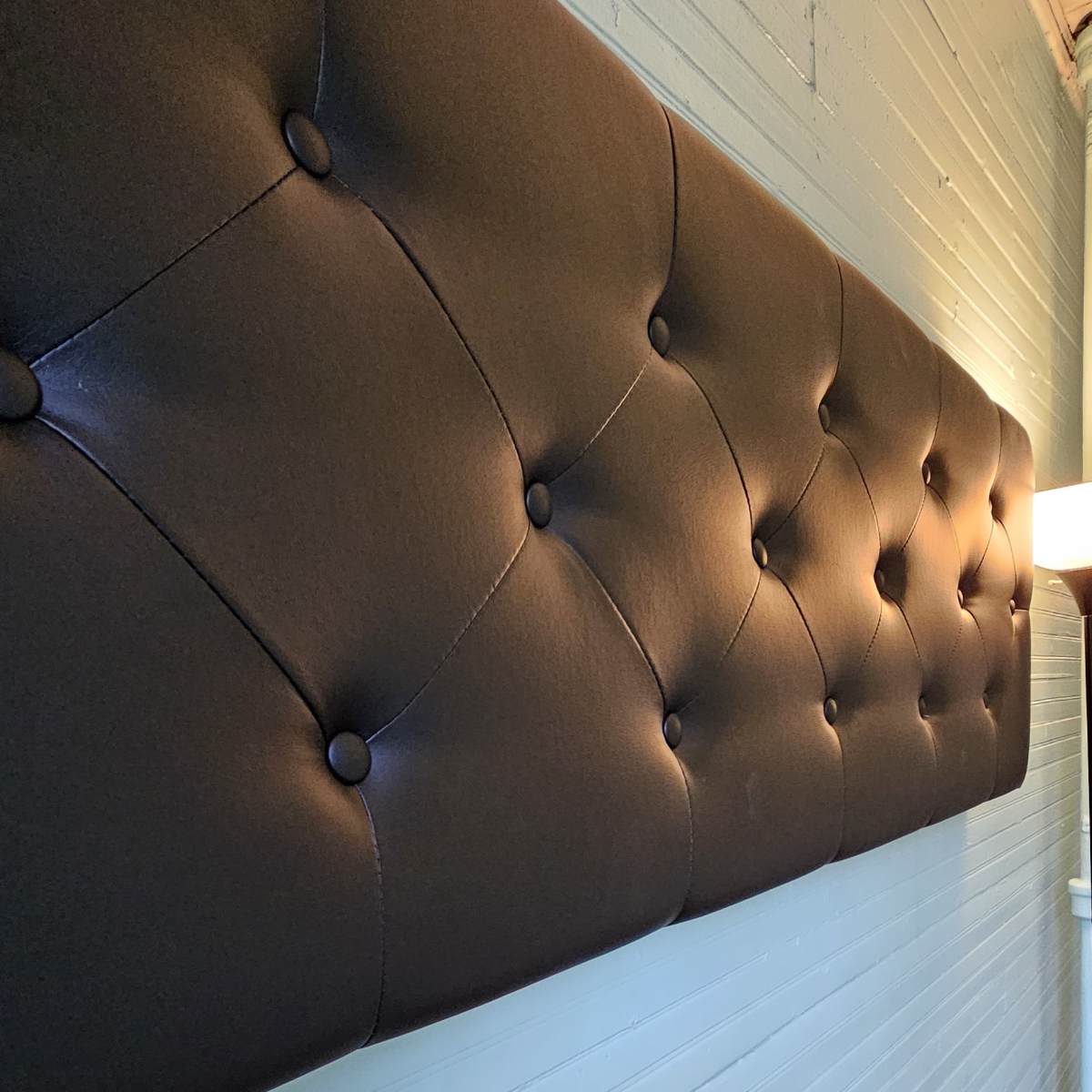 A long, black tufted headboard mounted against a light blue wall with wooden flooring visible below.