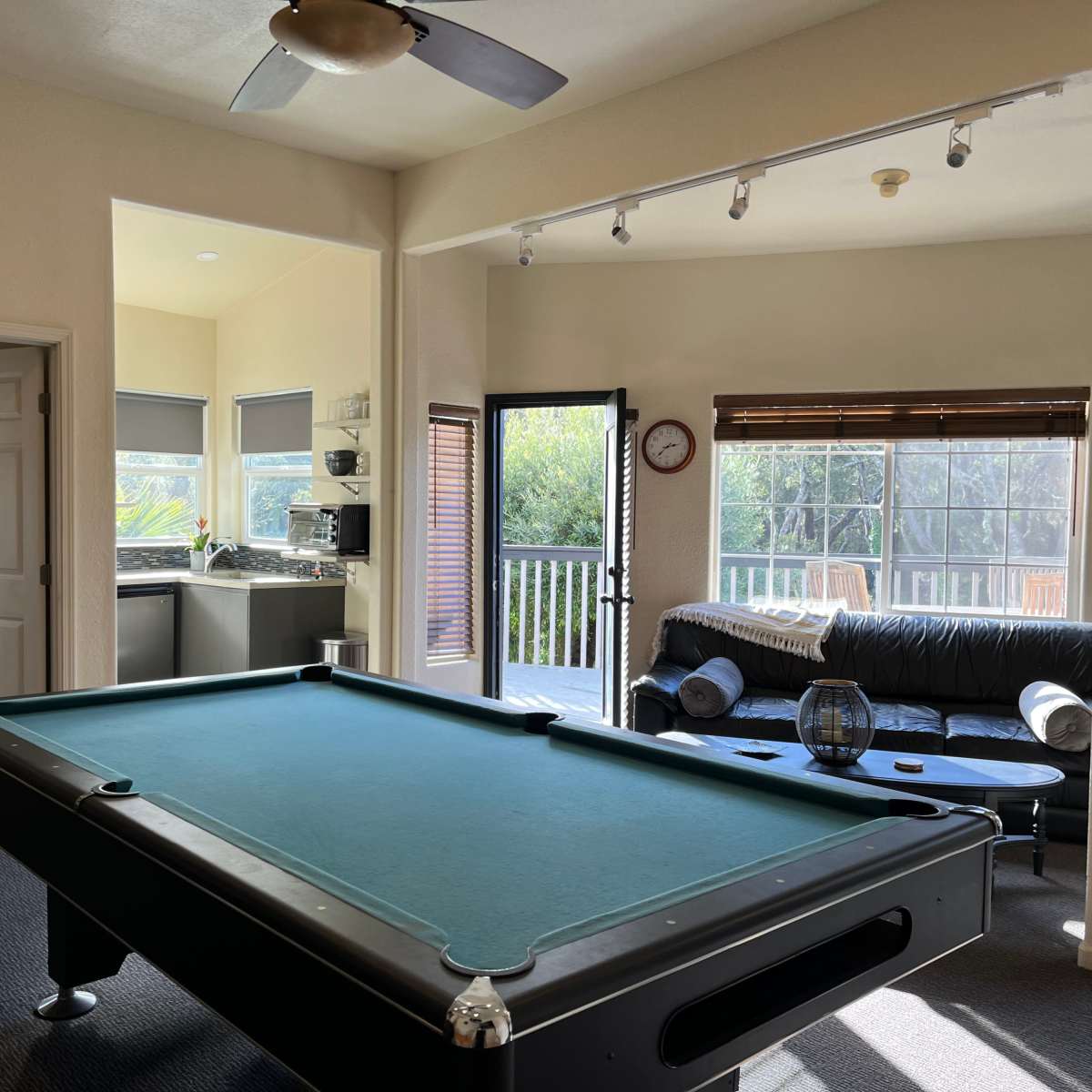 A spacious living area with a pool table, a sofa, and a kitchen accessible through an open doorway.