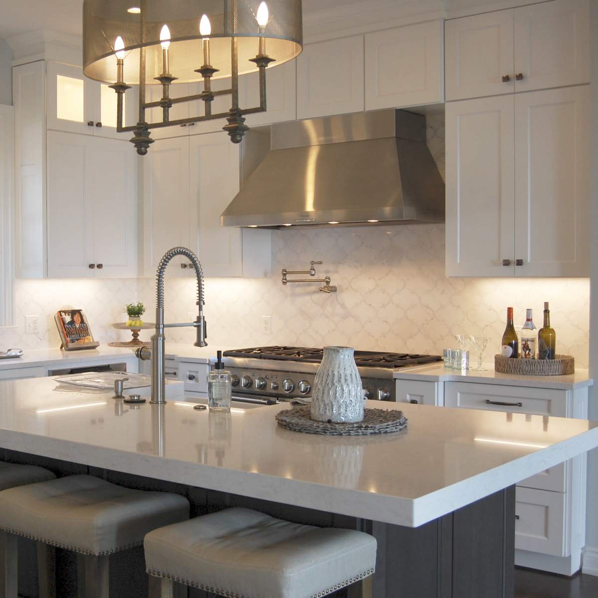 A modern kitchen featuring white cabinetry, a large central island with bar stools, stainless steel appliances, and a chandelier above the island.