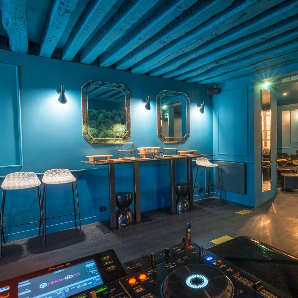 A blue-walled room with modern bar stools, mirrors, and a DJ turntable in the foreground.