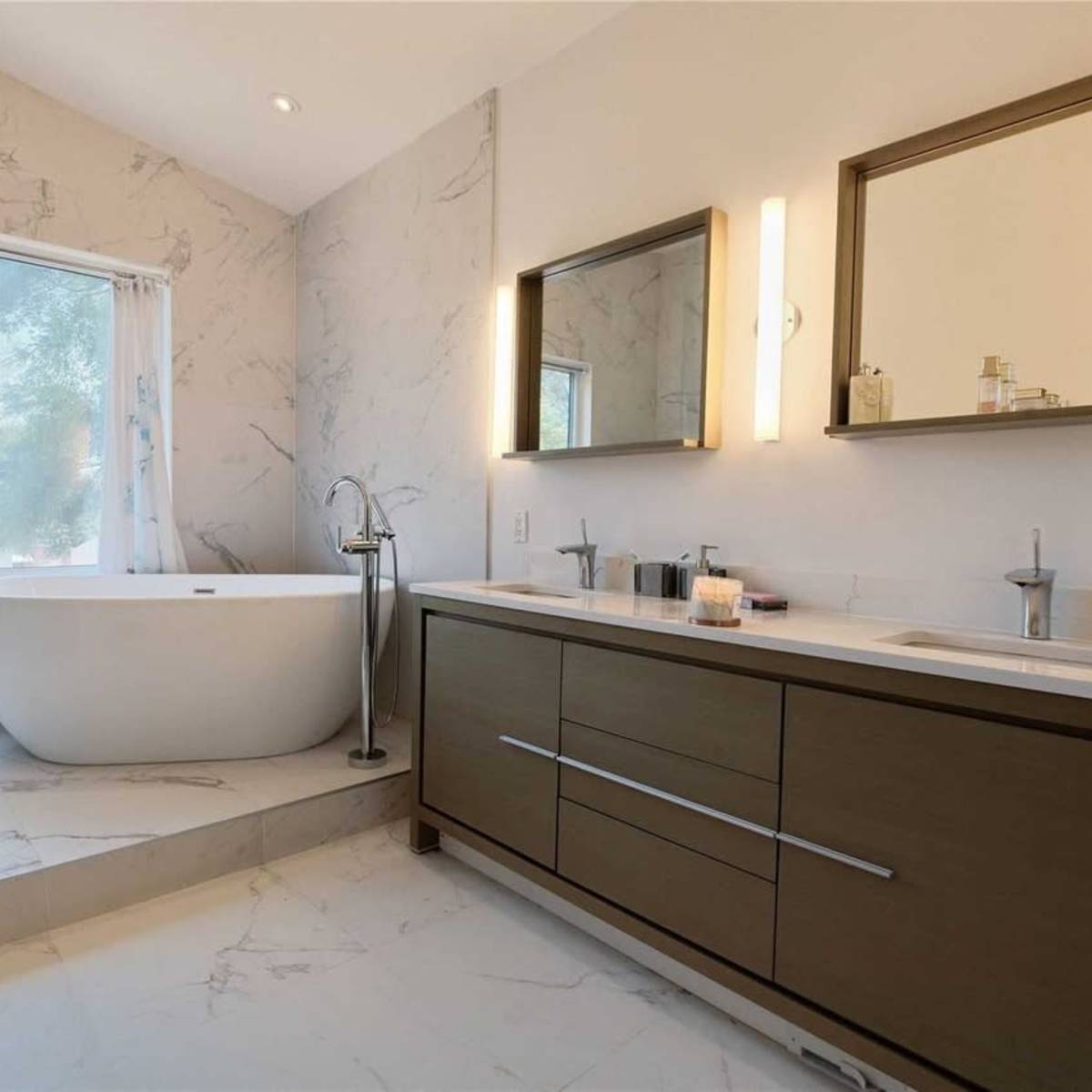 A modern bathroom featuring a freestanding bathtub, a double vanity with two sinks, and large windows allowing natural light to enter.