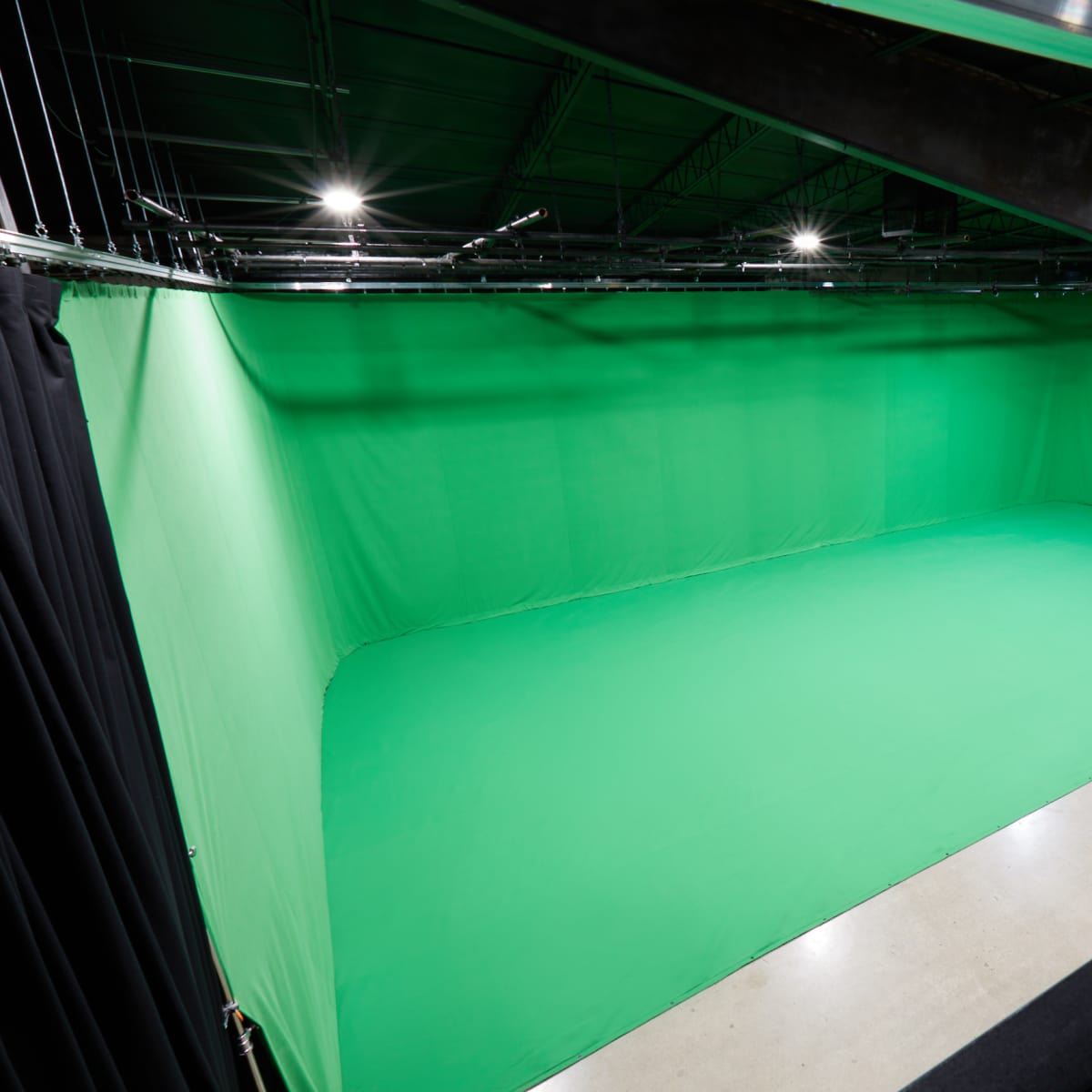 A spacious green screen studio with evenly lit green fabric walls and a smooth concrete floor.