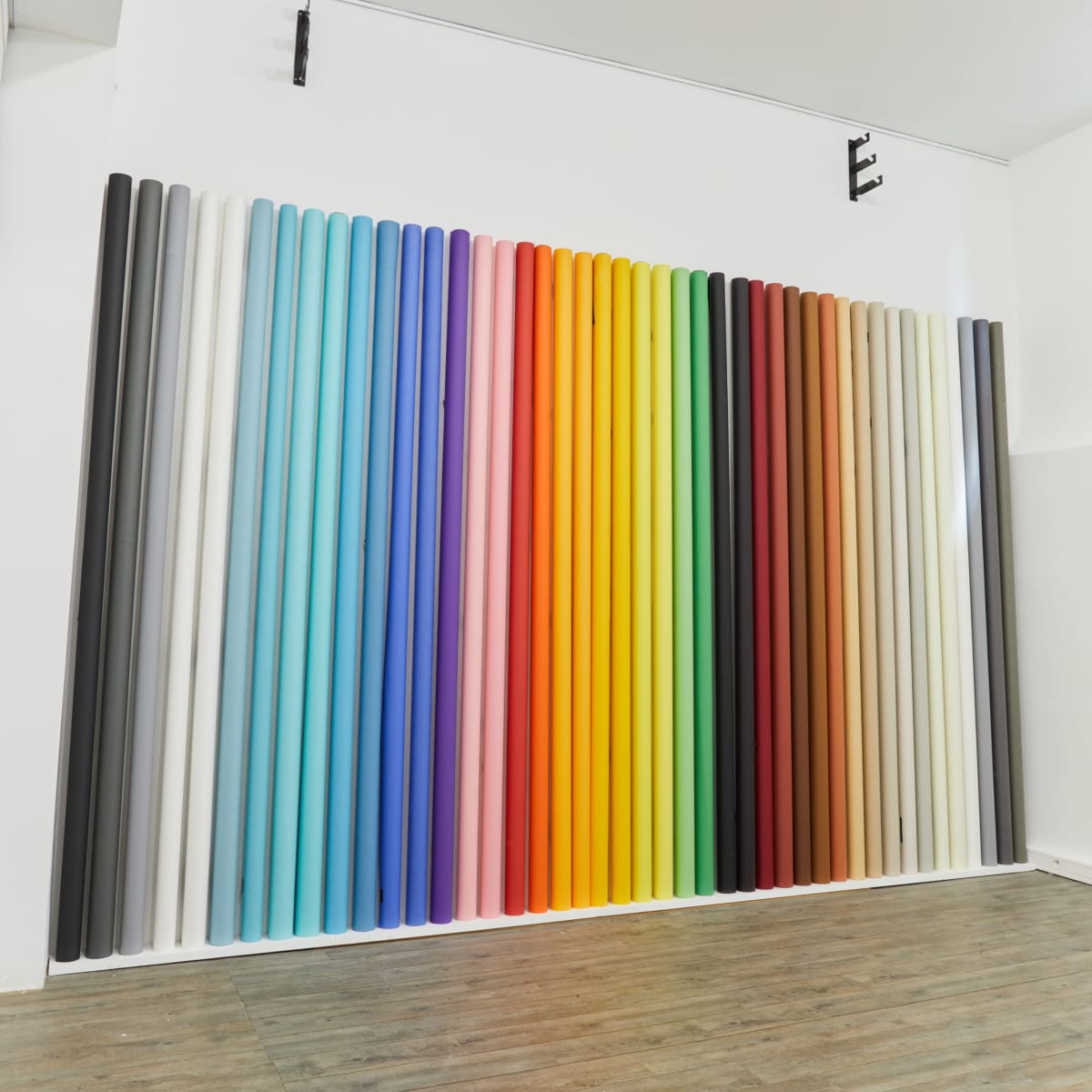 A wall covered with vertical rolls of colored paper arranged in a gradient from dark to light shades.