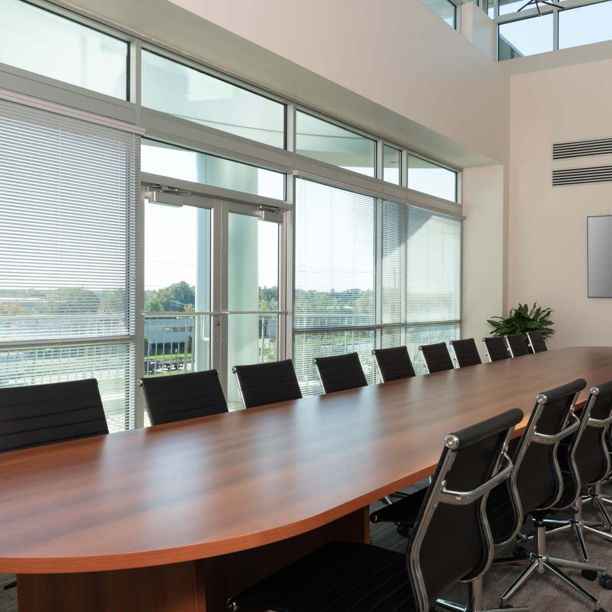 A large conference room features a wooden table surrounded by black chairs, with floor-to-ceiling windows letting in natural light.