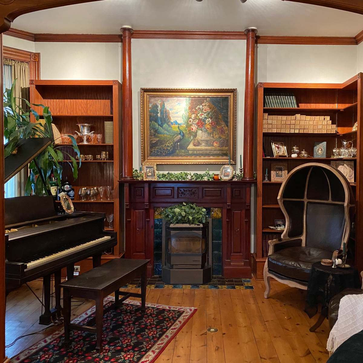 A living room with a grand piano, a fireplace surrounded by bookshelves, and a large painting on the wall.